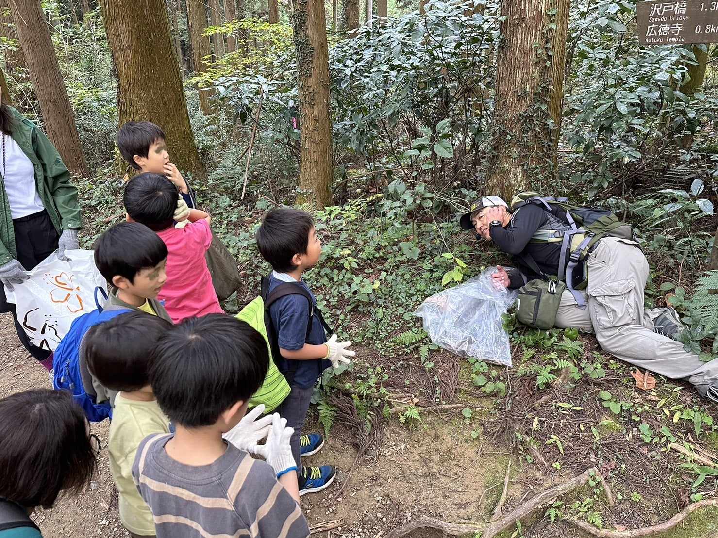 森の中でガイドが寝転んで実演し、子どもたちが見つめている